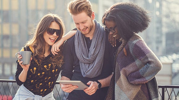 Three people outside reading on a tablet Three young people outside smiling and reading on a tablet