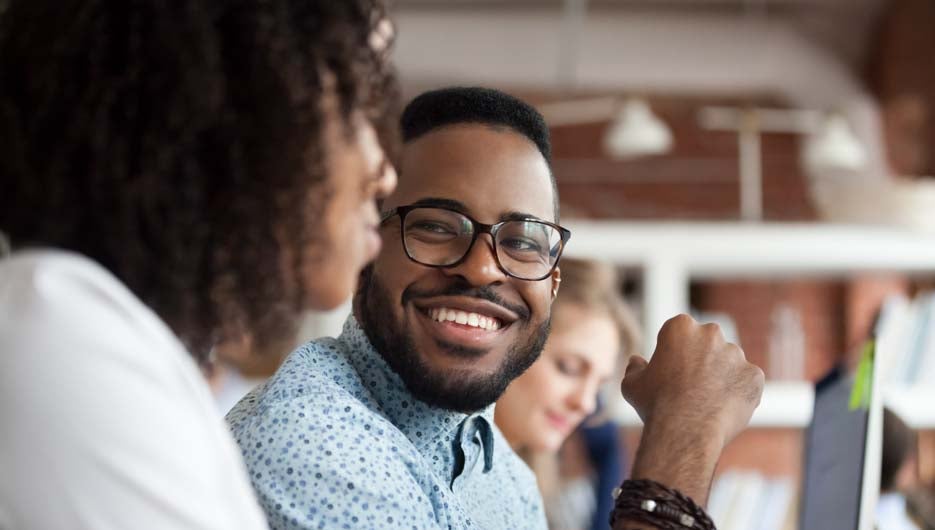 Close up of smiling African American employee look at female colleague chatting in office, happy black male worker talk with woman coworker, having casual conversation at workplace, have fun