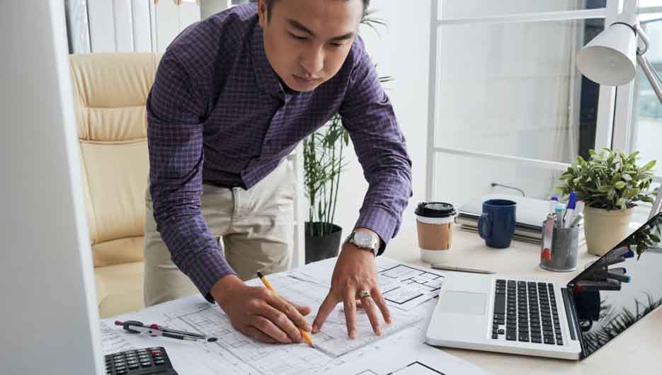 Professional Vietnamese construction engineer checking details in blueprint